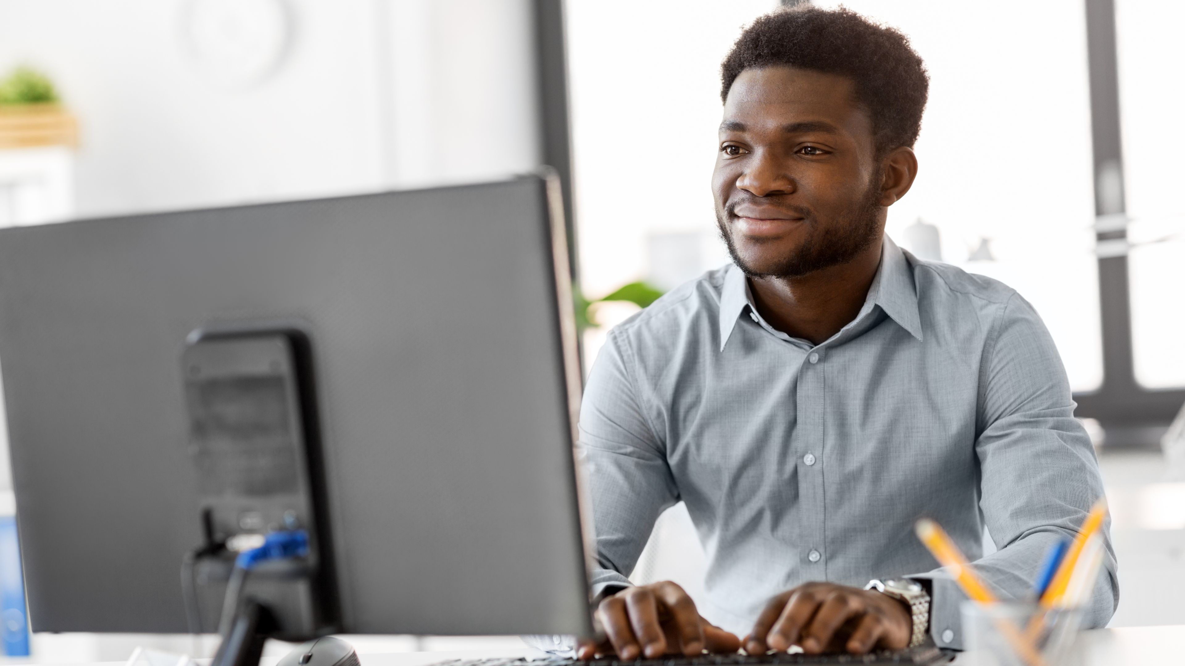 Developer smiling while typing on a desktop keyboard at a bright modern office workspace