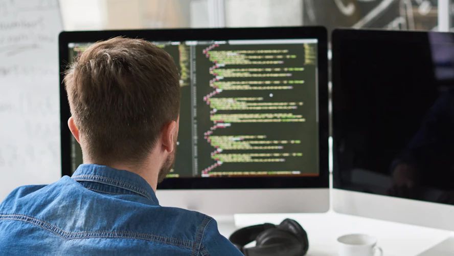 Developer working at dual monitors displaying lines of code