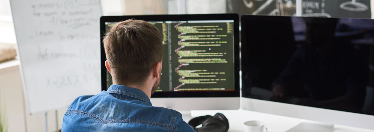 Developer working at dual monitors displaying lines of code