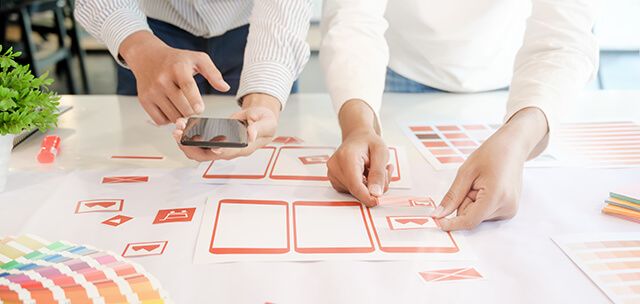 Two people arranging mobile UI wireframe cards and color swatches on a table
