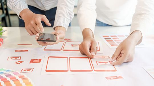Two people arranging mobile UI wireframe cards and color swatches on a table