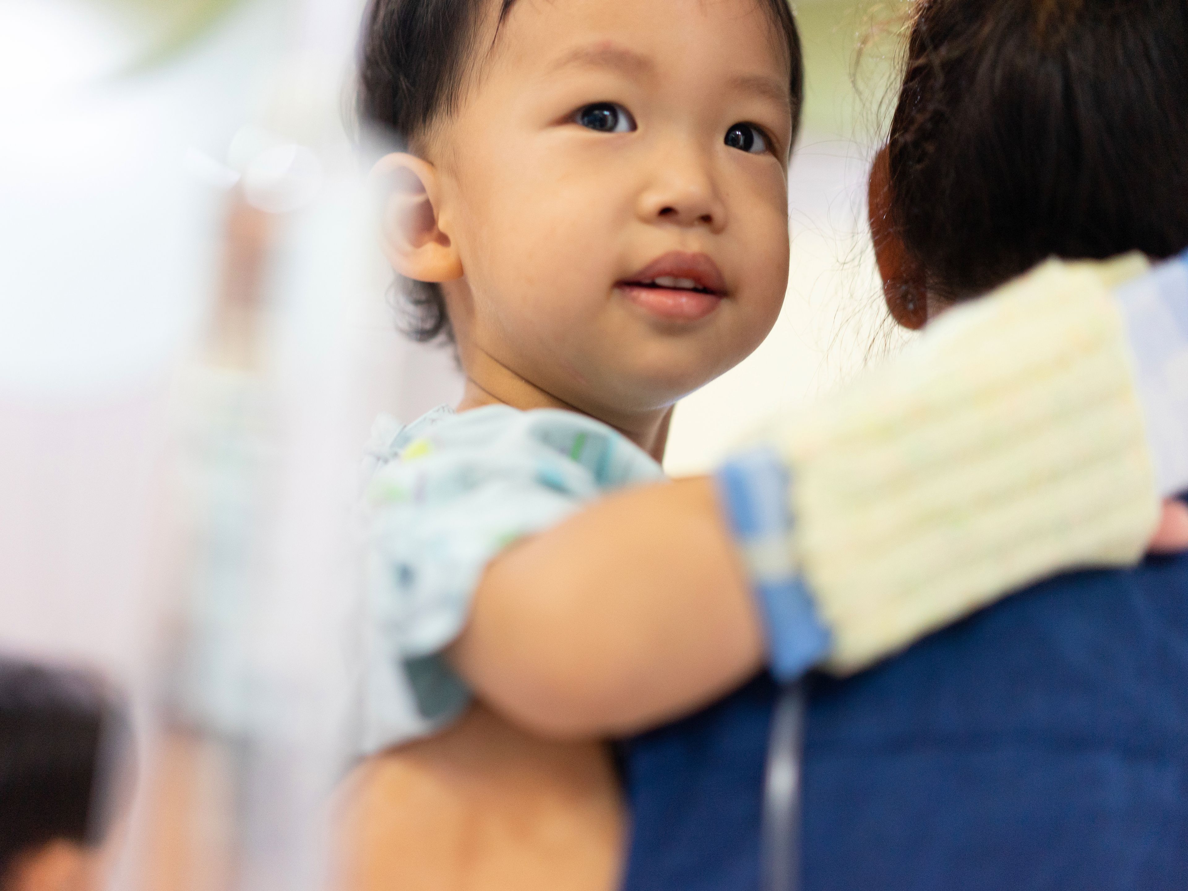 Young child with a hospital wristband held by a caregiver, looking over their shoulder with a gentle expression