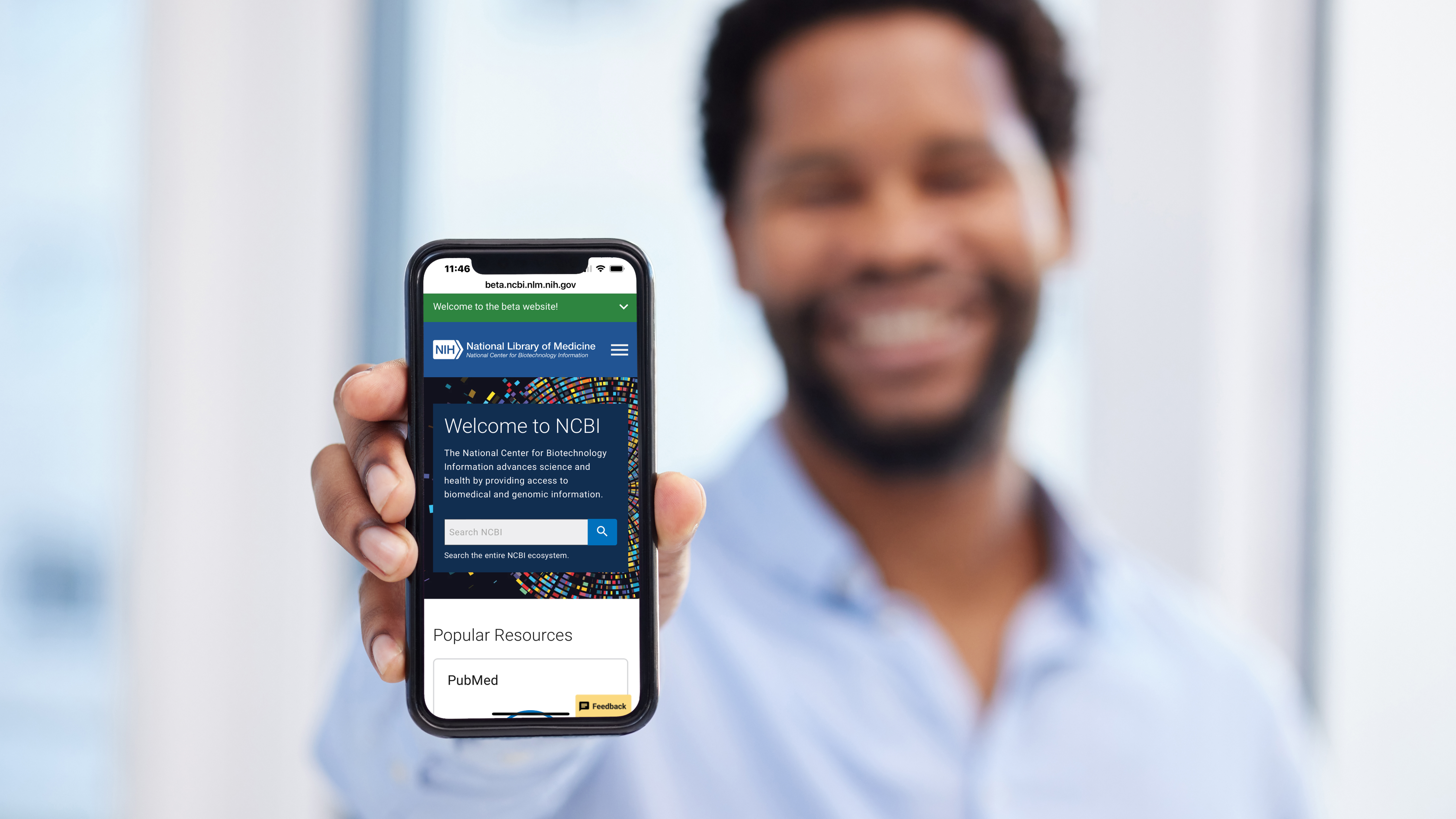 Person holding a smartphone displaying the NCBI website homepage with its search interface and Popular Resources section