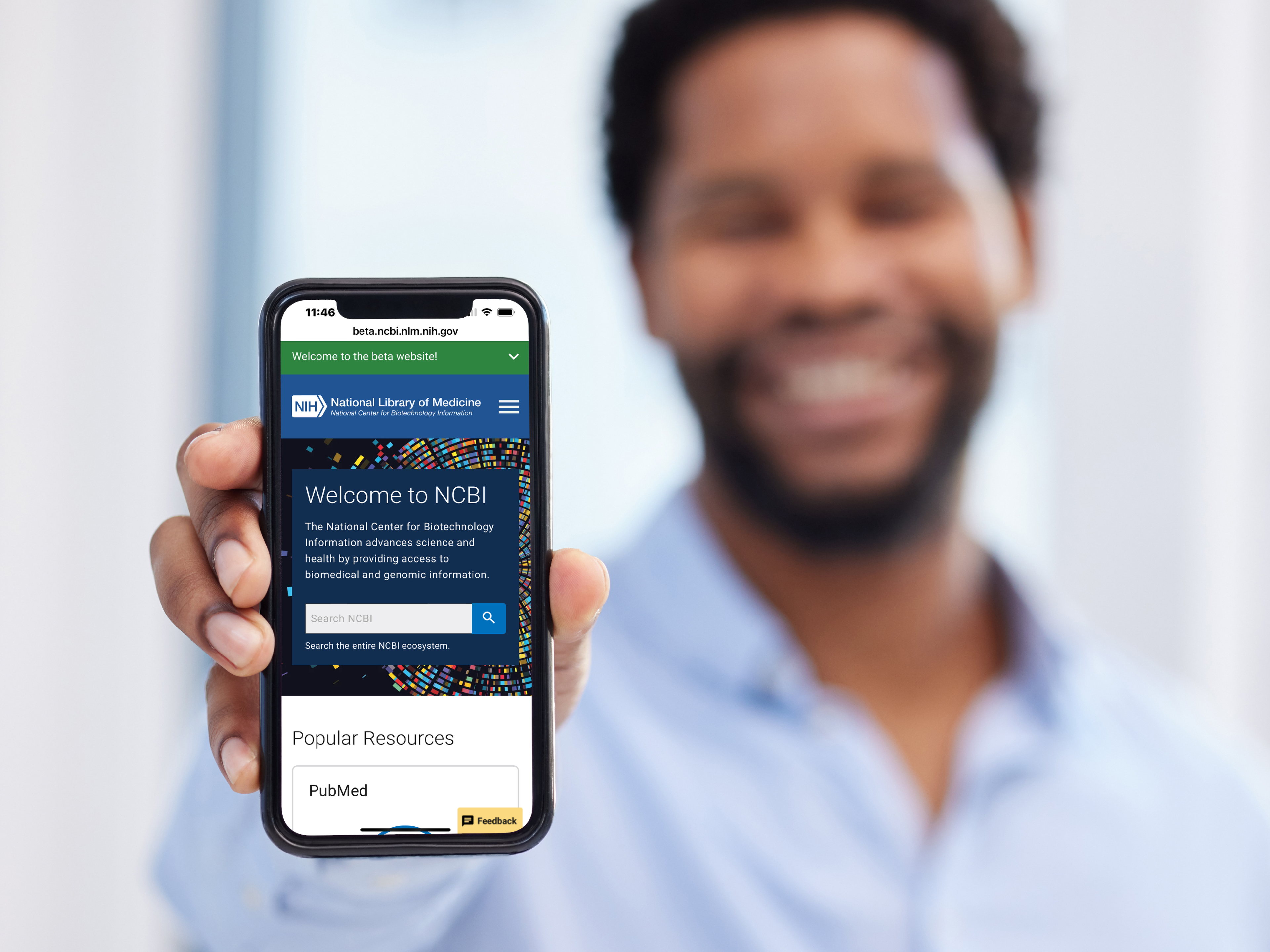 Person holding a smartphone displaying the NCBI website homepage with its search interface and Popular Resources section