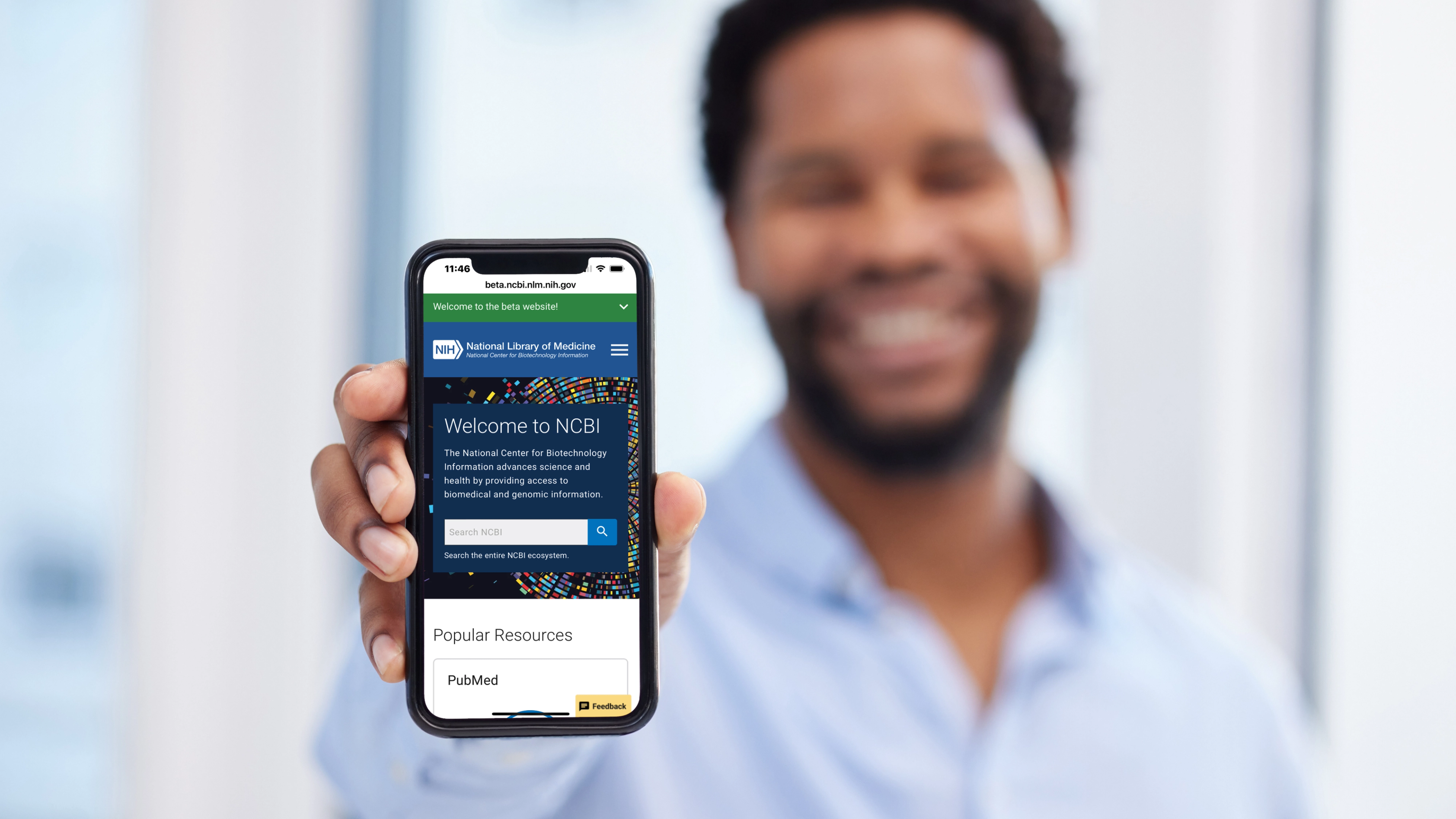 Person holding a smartphone displaying the NCBI website homepage with its search interface and Popular Resources section