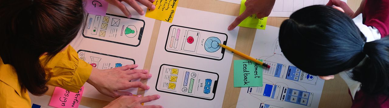 Team sketching mobile app wireframes with sticky notes on a large paper