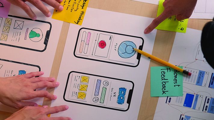 Team sketching mobile app wireframes with sticky notes on a large paper