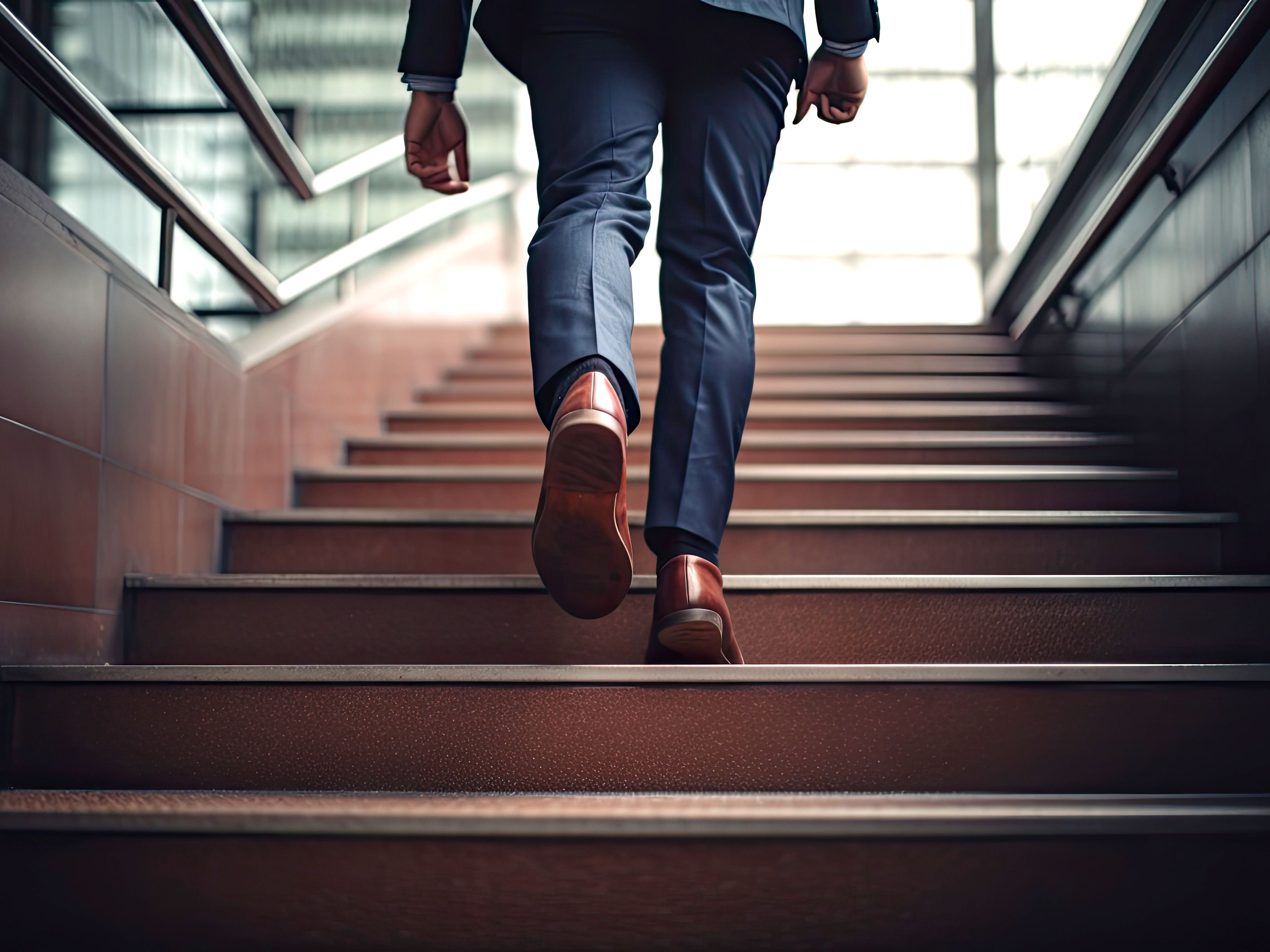 Business professional ascending a modern staircase in dress shoes and slacks, viewed from a low angle in an office building