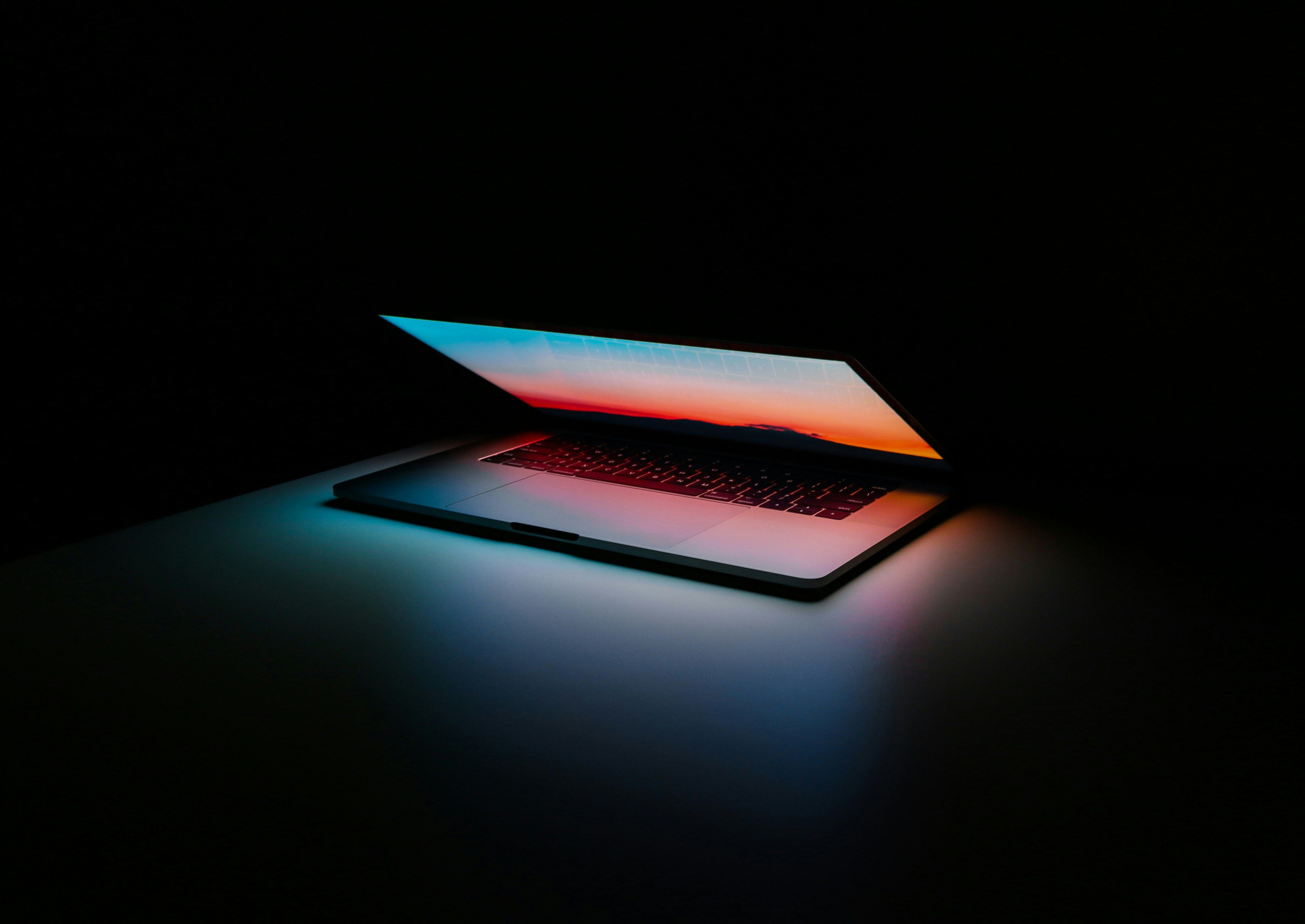 Laptop half-open in a dark room, its screen casting a colorful glow