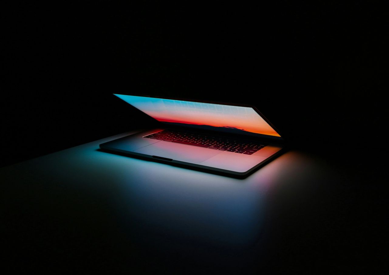 Laptop half-open in a dark room, its screen casting a colorful glow