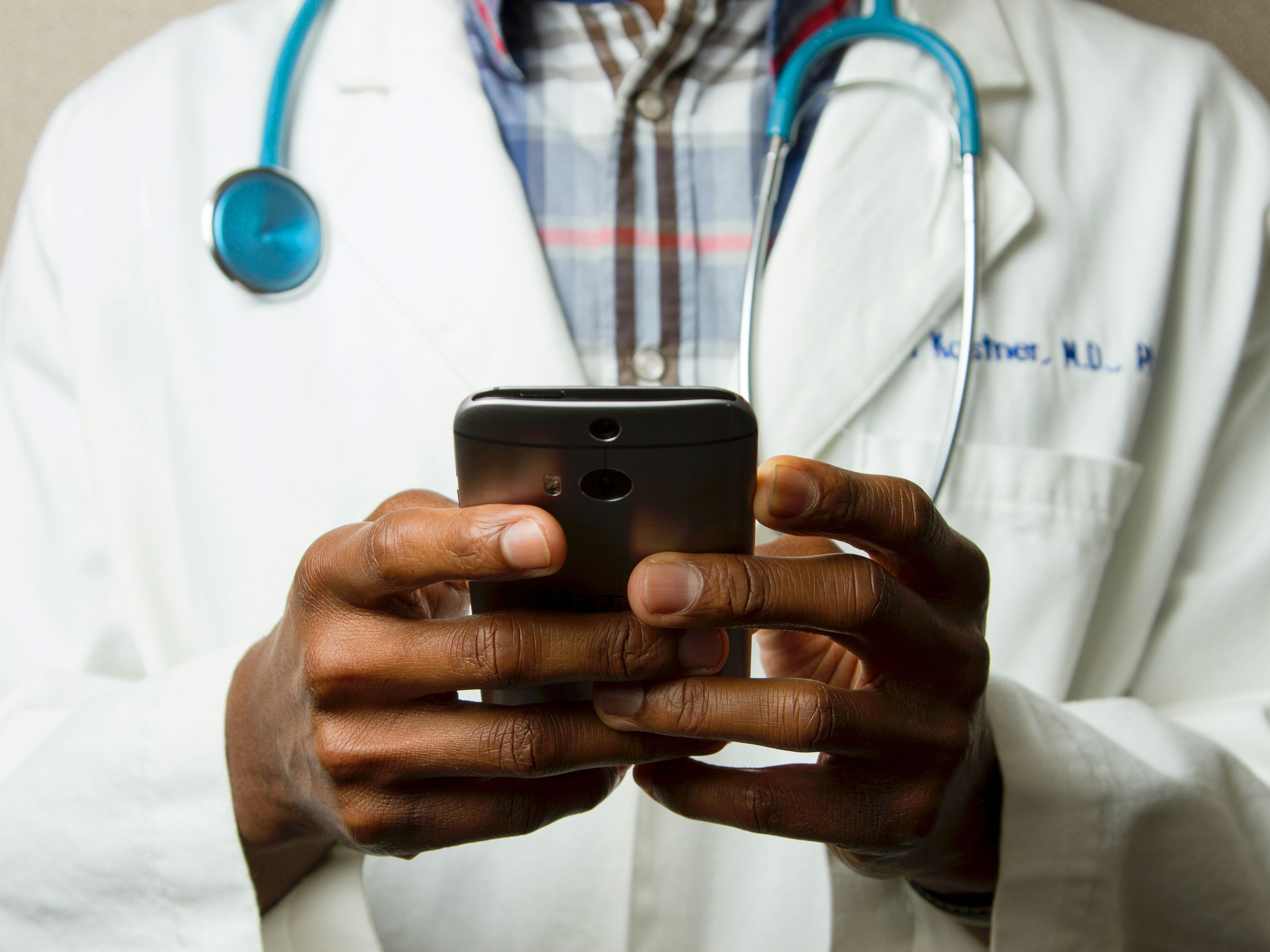 Healthcare provider in a white coat and stethoscope using a smartphone, representing digital health engagement