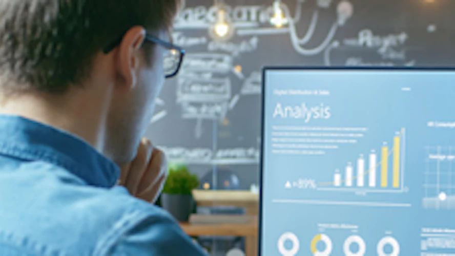 Professional reviewing analytics dashboards with bar charts and graphs on a desktop monitor