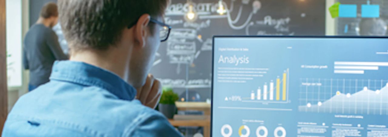 Professional reviewing analytics dashboards with bar charts and graphs on a desktop monitor