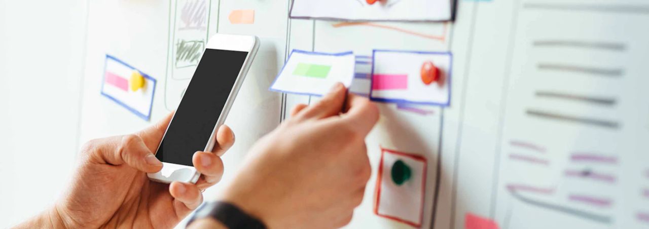 Designer holding a smartphone while reviewing UI component cards on a whiteboard