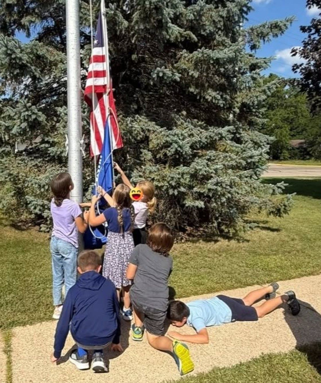 Fifth graders raising the flags while classmates lie on the ground beneath them as a “human rug.”