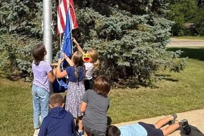 Fifth graders raising the flags while classmates lie on the ground beneath them as a “human rug.”