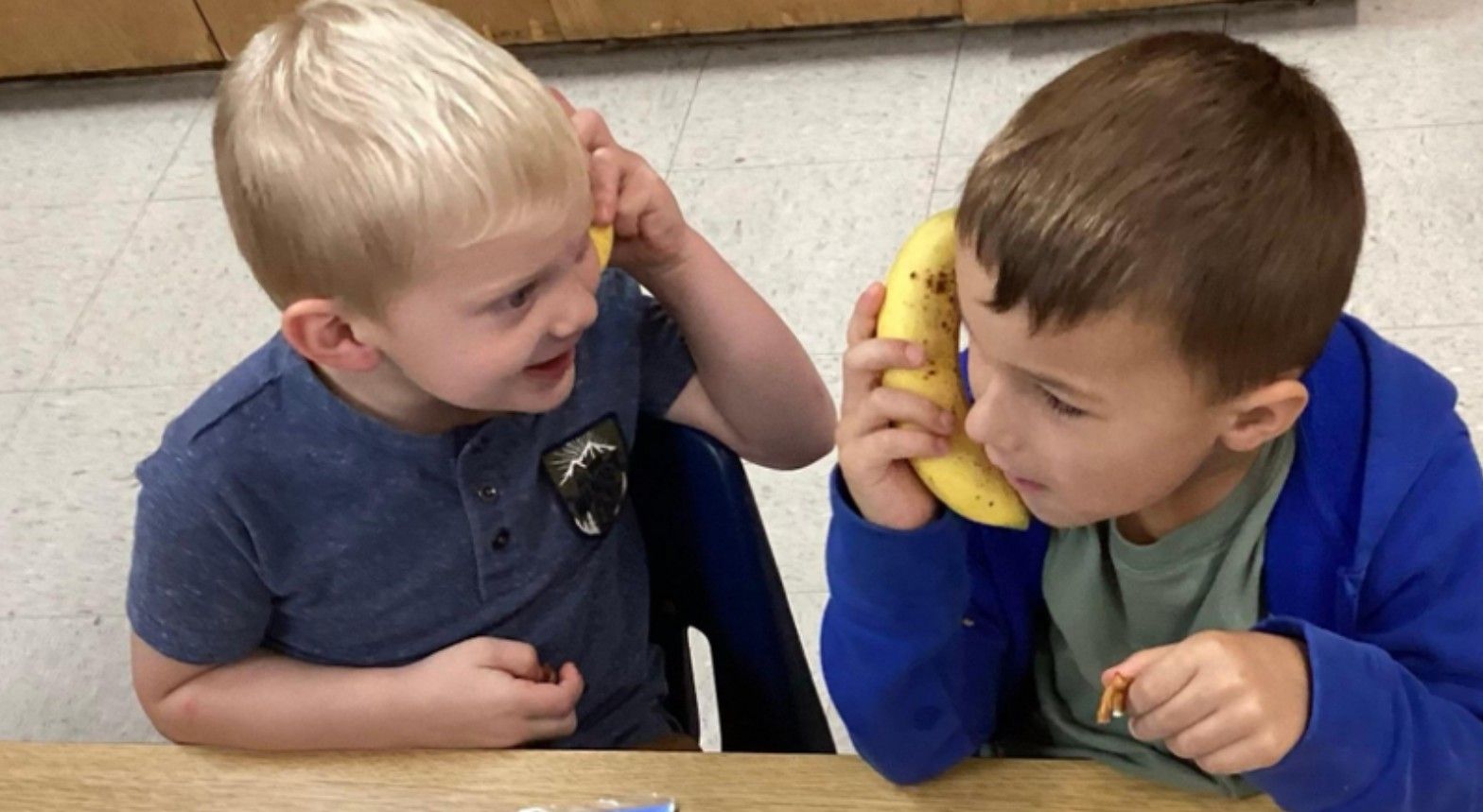 Two preschoolers pretending a banana is a phone at snack time.