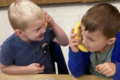 Two preschoolers pretending a banana is a phone at snack time.