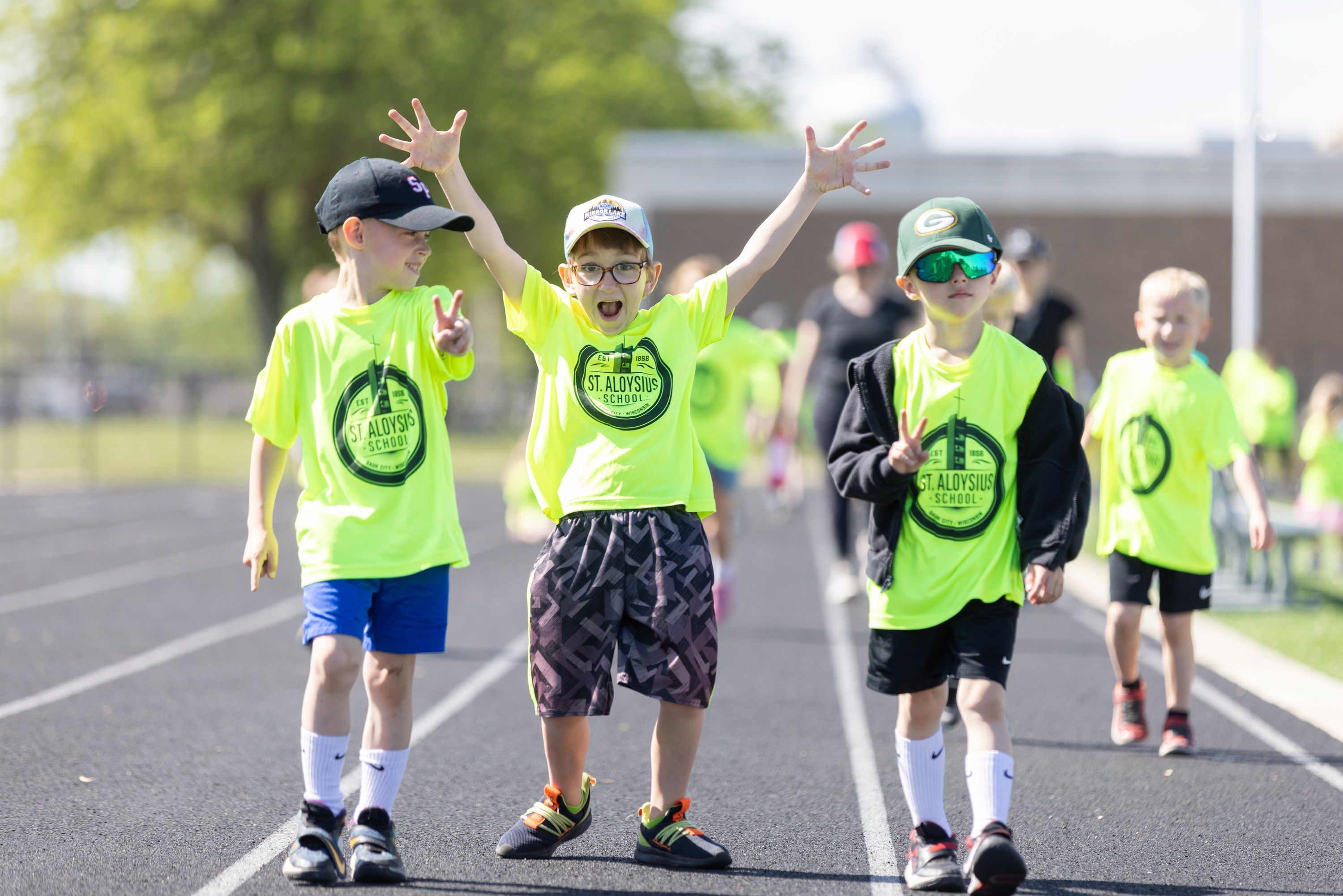Three young students cheer with their arms up as they walk the track at the 2025 Walk for Goodness' Sake.