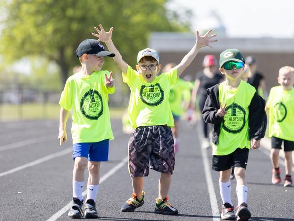 Three young students cheer with their arms up as they walk the track at the 2025 Walk for Goodness' Sake.
