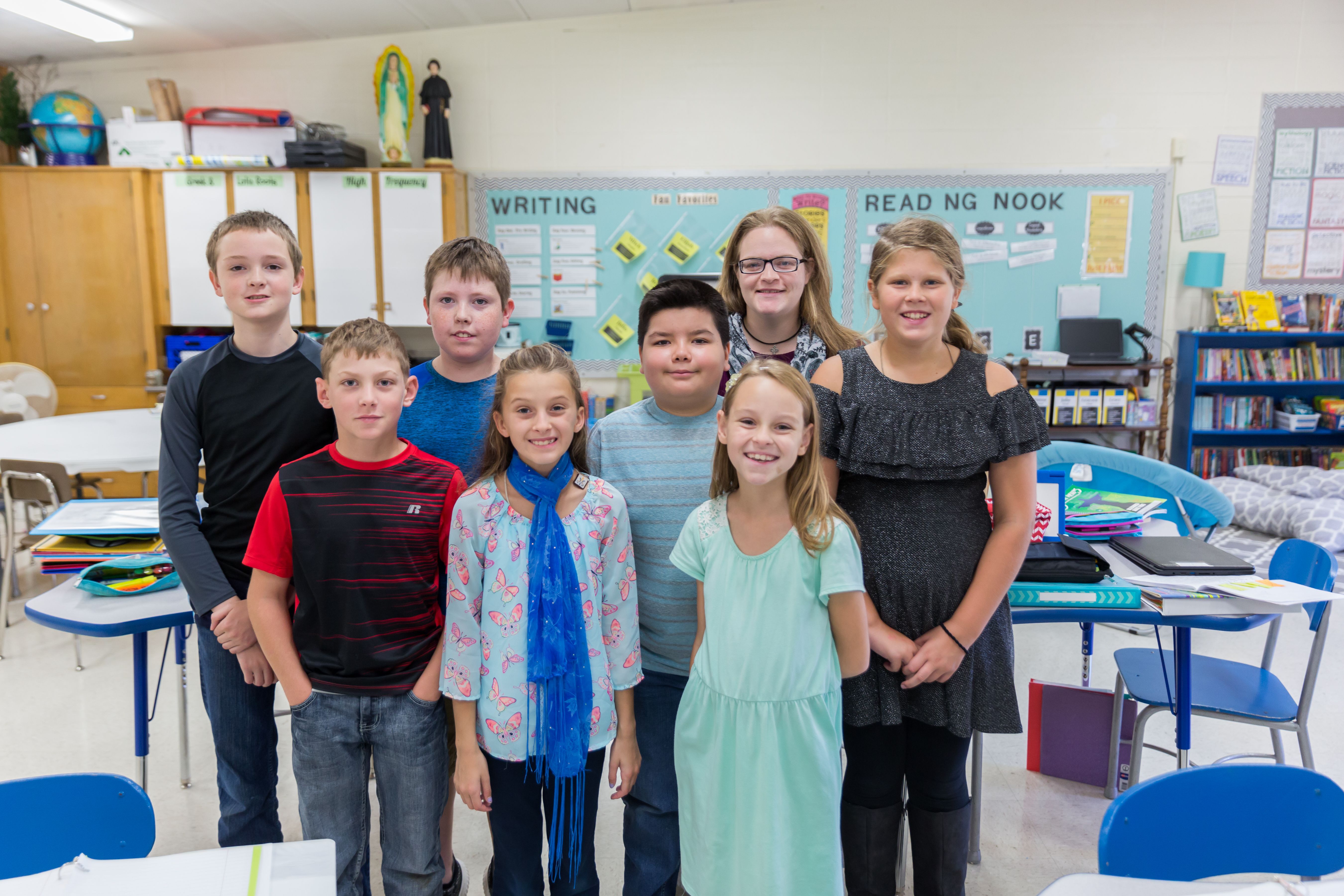 A group of smiling students stand with their teacher in a classroom.