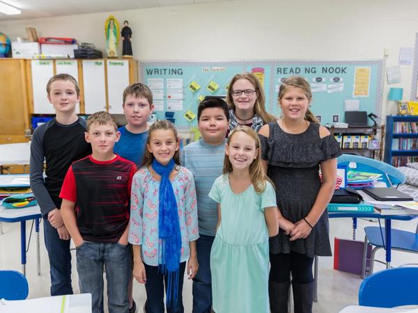 A group of smiling students stand with their teacher in a classroom.