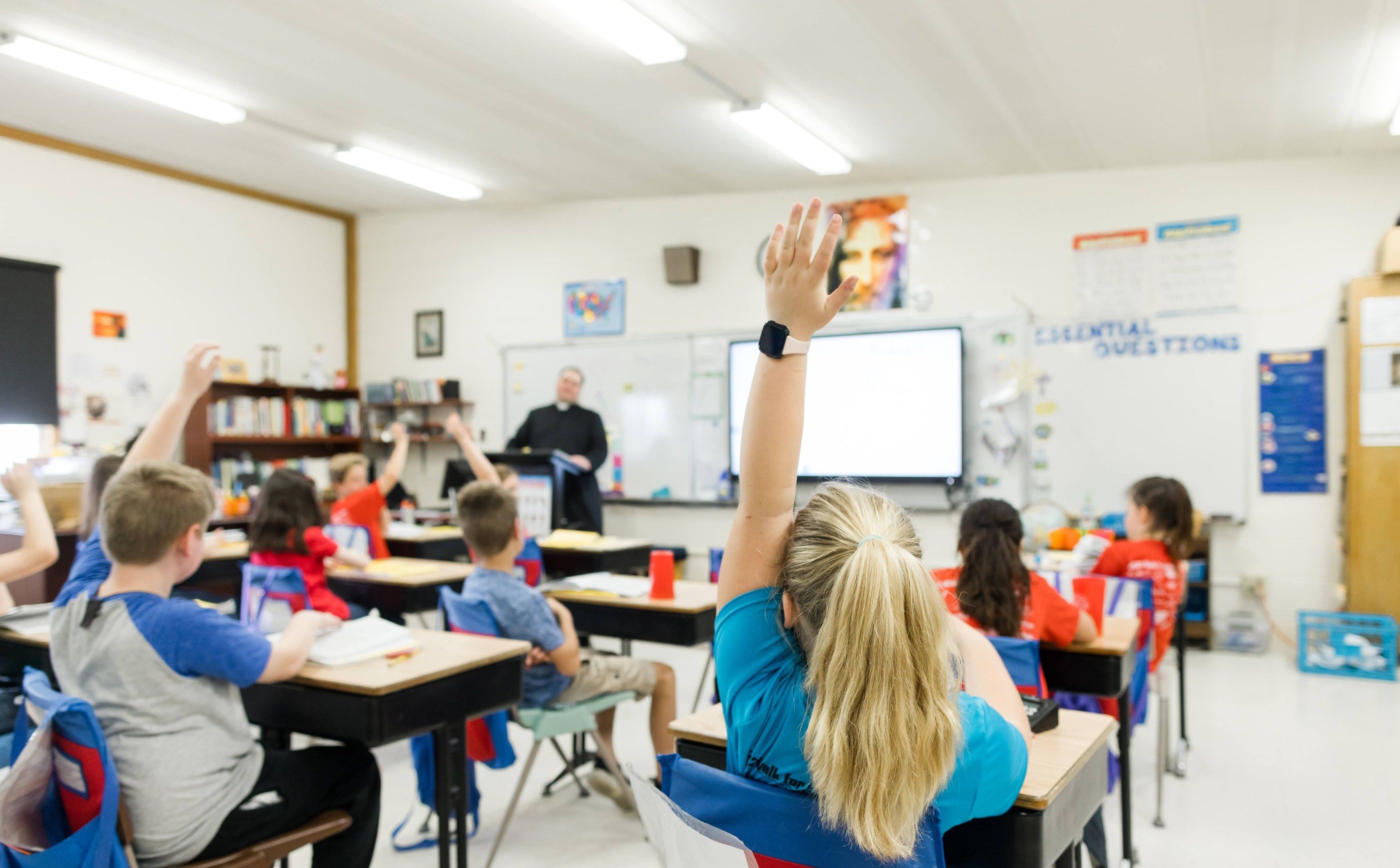 Older students raise their hands during a lesson in a bright classroom.