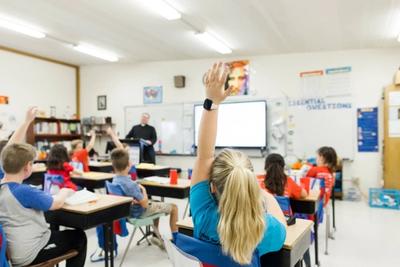 Older students raise their hands during a lesson in a bright classroom.