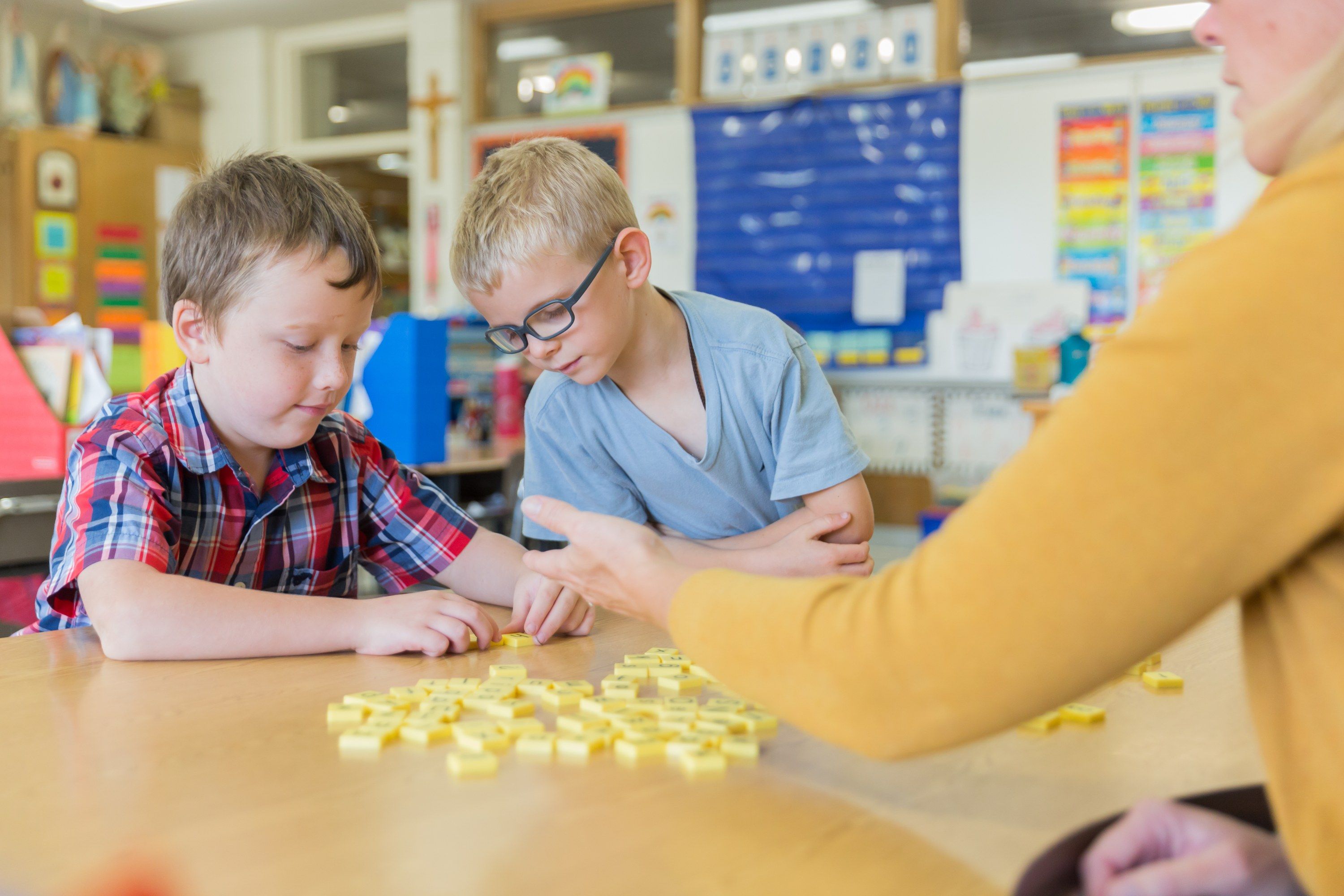 Two students count with yellow tiles as their teacher guides them at a small table.