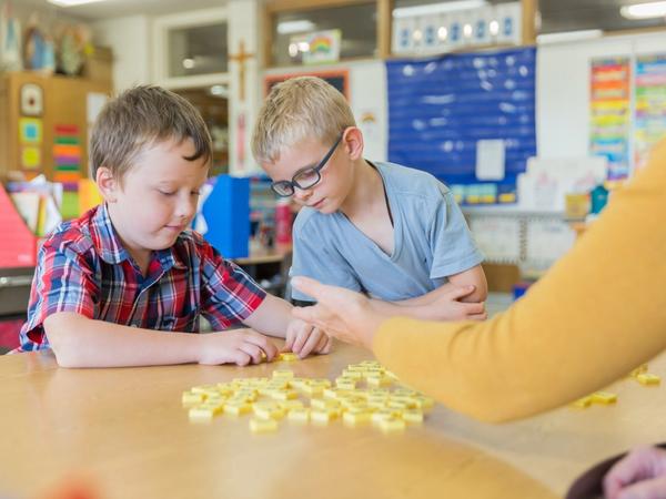 Two students count with yellow tiles as their teacher guides them at a small table.