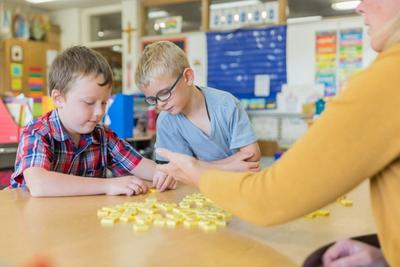 Two students count with yellow tiles as their teacher guides them at a small table.