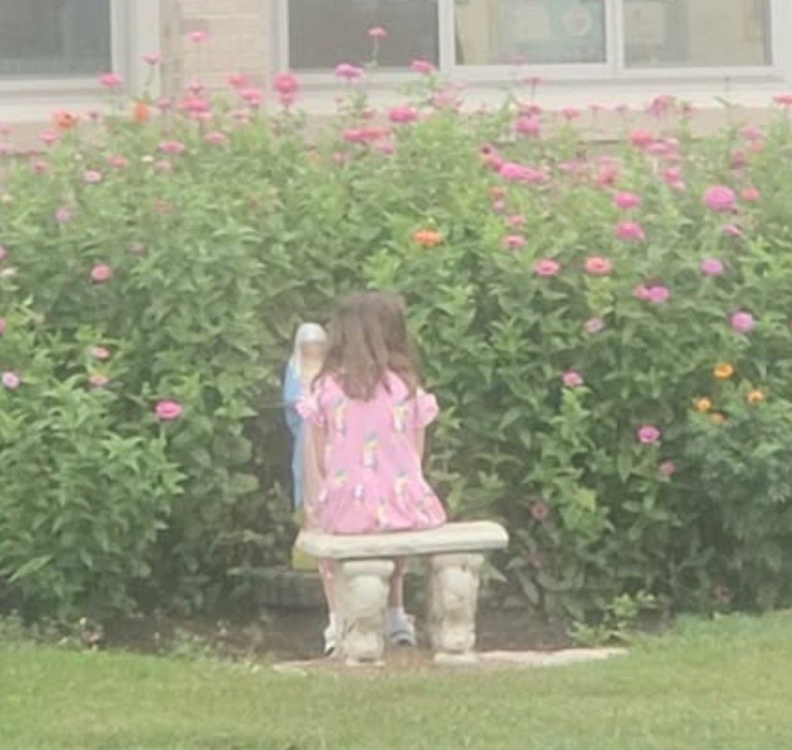 A student sitting on a bench in the flowering Mary Garden at recess.