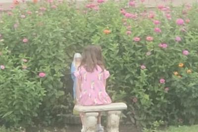A student sitting on a bench in the flowering Mary Garden at recess.