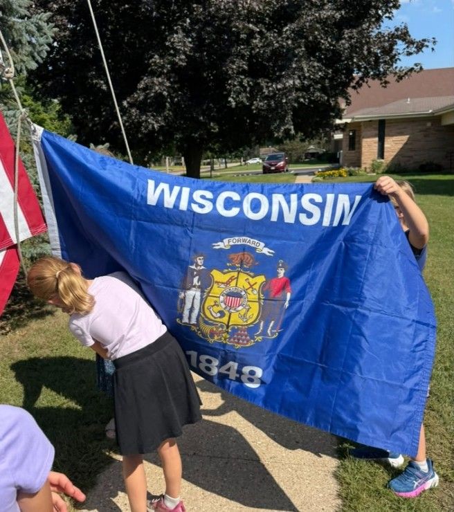 Students holding the Wisconsin state flag outside the school.