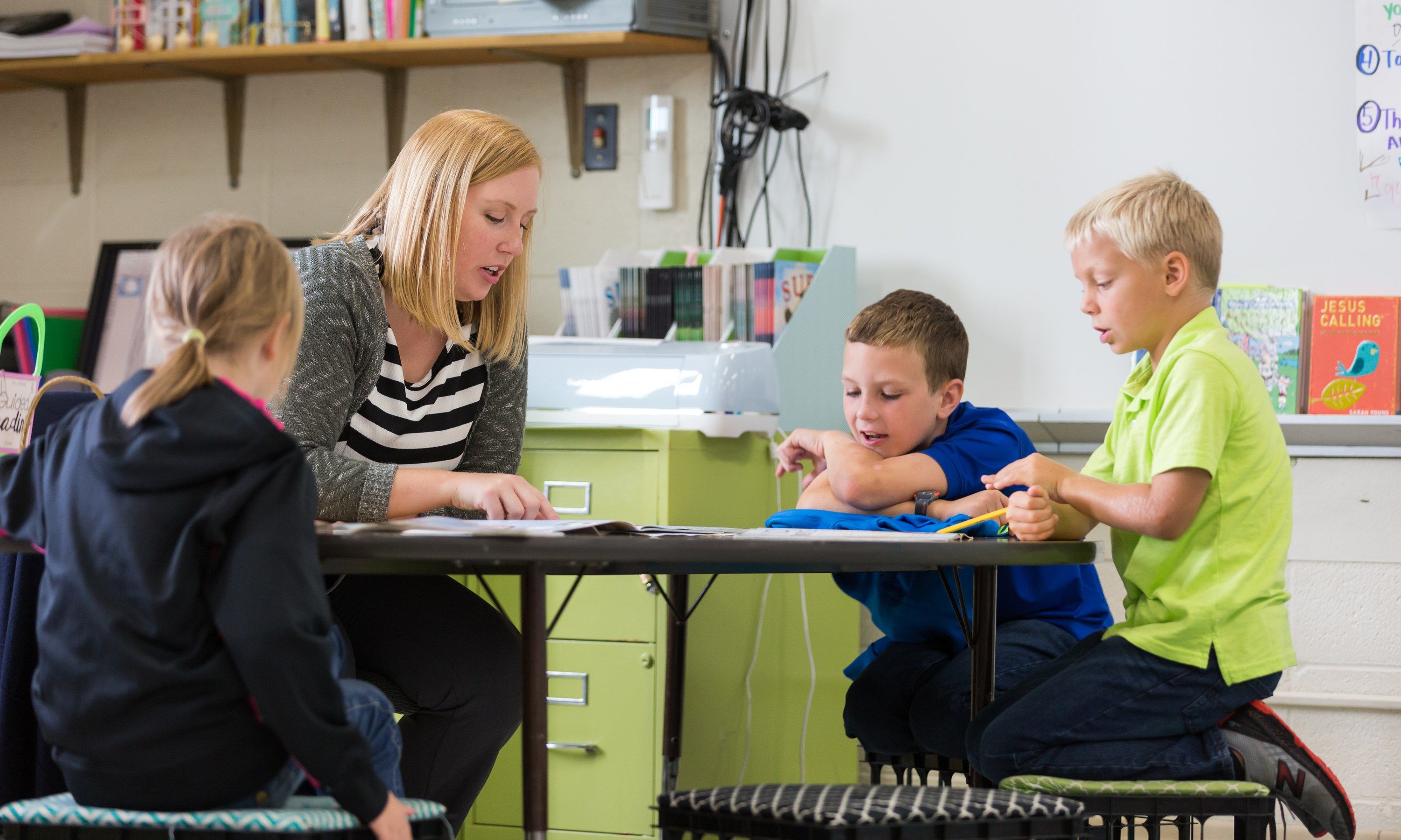 A teacher reads with three students around a small table in her classroom.