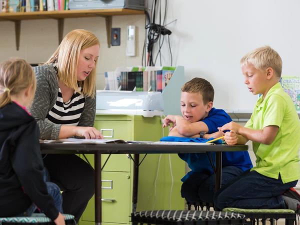 A teacher reads with three students around a small table in her classroom.