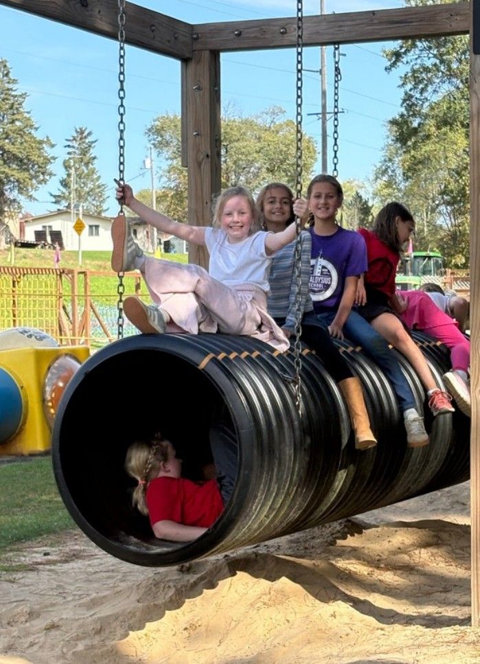 Students playing on a big tire tunnel at the farm playground.