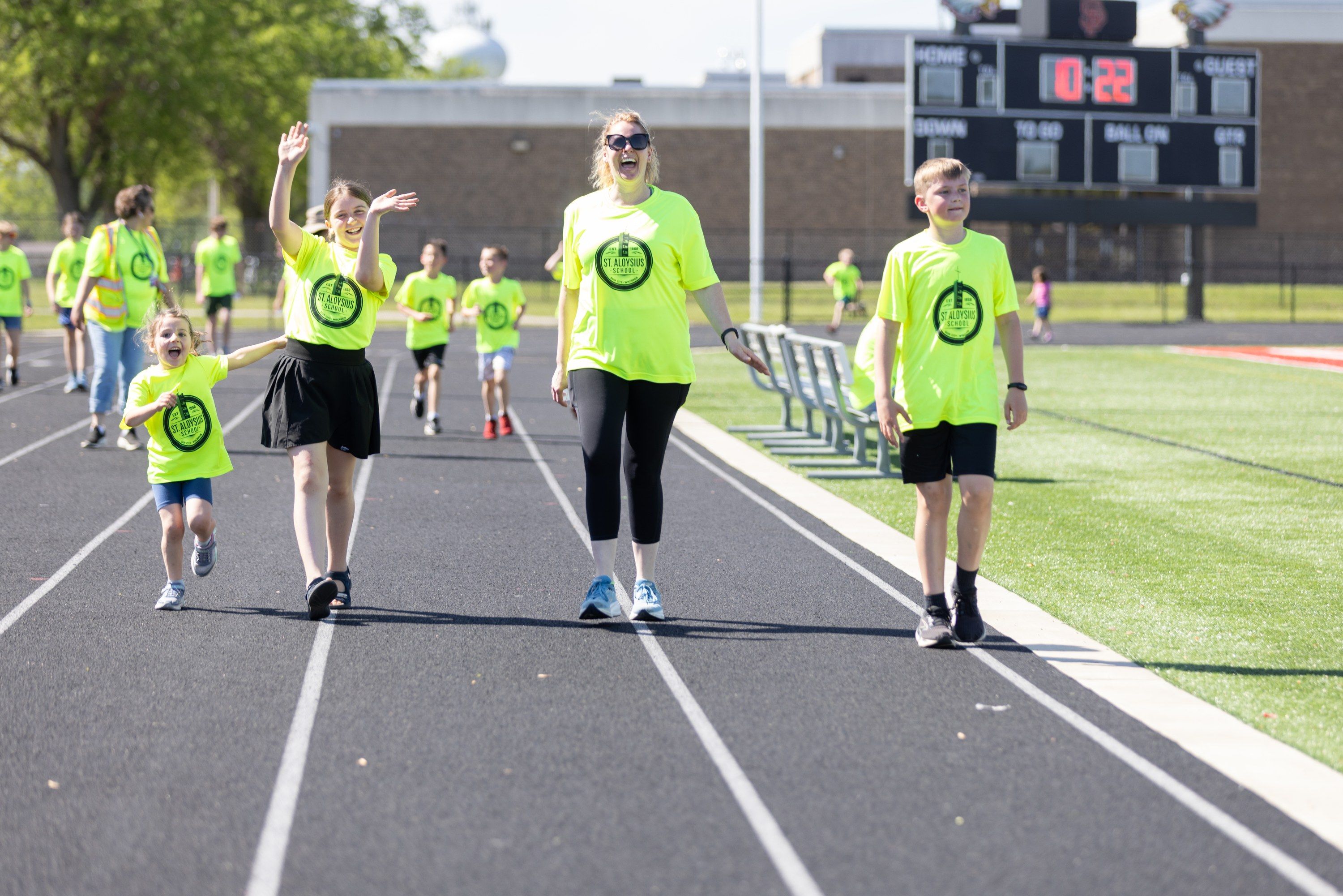 Students and an adult wave and laugh as they walk the track together at the 2025 Walk for Goodness' Sake.