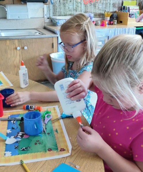 Two students gluing paper pieces onto an art project.