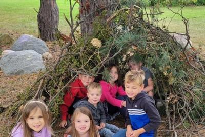 Kindergartners sitting inside the cave they built from branches.