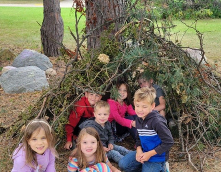 Kindergartners sitting inside the cave they built from branches.