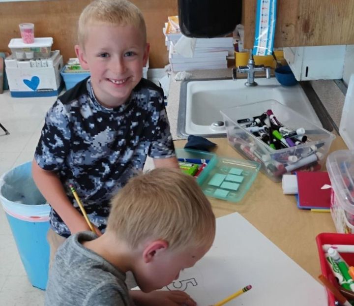 Two first graders coloring their poster at a classroom table.