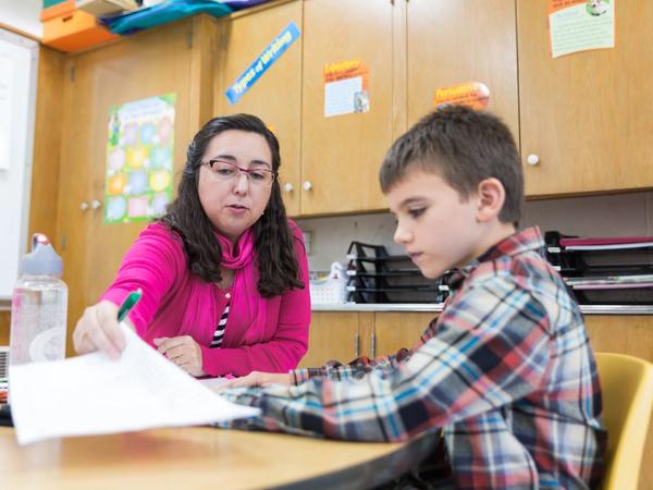 A teacher reviews a student's writing with him one-on-one at her desk.