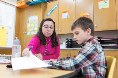 A teacher reviews a student's writing with him one-on-one at her desk.