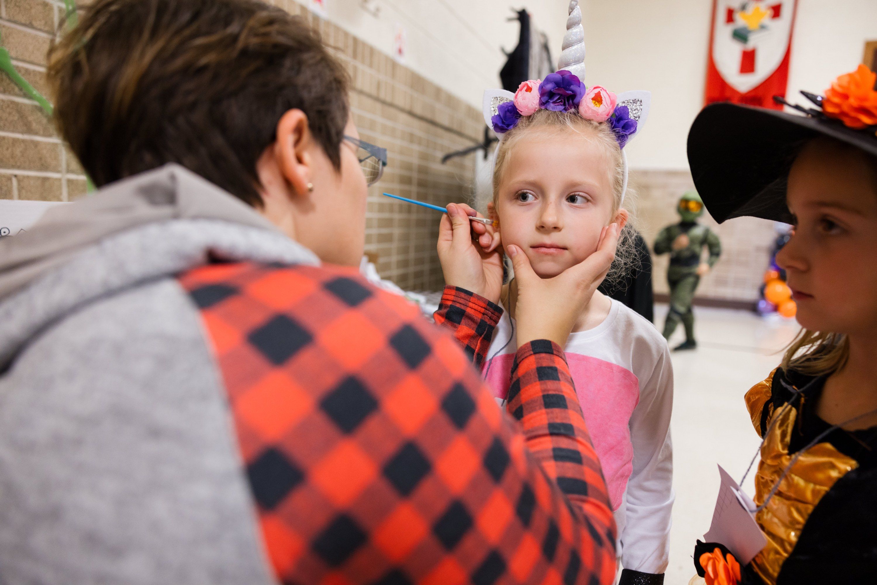 A volunteer paints a design on a young student's cheek at the all-school Halloween party.
