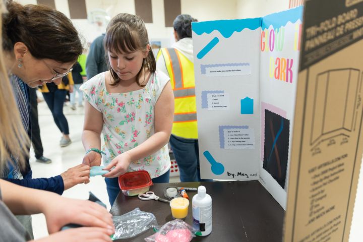 Meg Brickl (not in photo) and Savannah Ziegler show Principal Miss Daniela how to make glow-in-the-dark slime!
