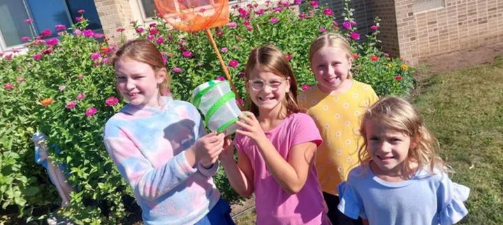 Students with bug catchers and a net in a flower garden.