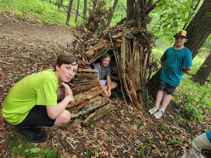Connor Kendall and Calvin Breunig admire the shelter they built, while Vos Betley gives it a try.