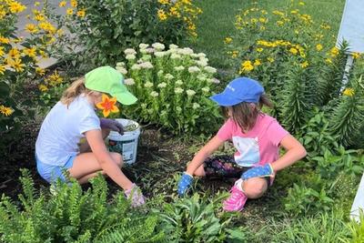 Two students weeding a flower bed in front of the school.