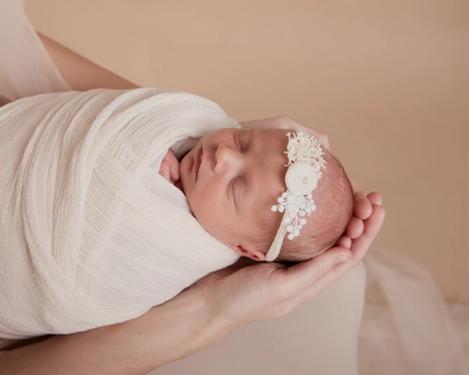 Baby with lace headband wrapped in light cloth in mother's hands